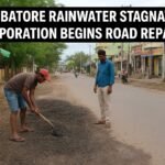 Municipal workers repairing a rain-damaged road in Coimbatore after heavy rainfall caused water stagnation, with shops and houses visible along the street.